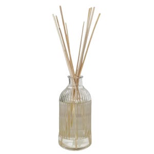Puede incluir: Un frasco difusor de caña de vidrio transparente con un diseño acanalado, lleno de líquido y rematado con varias cañas de madera de color claro. El frasco tiene una forma redondeada y un cuello estrecho, adecuado para la fragancia del hogar.