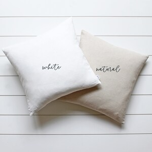 May include: Two square throw pillows, one white and one natural linen, with the words "white" and "natural" written in black cursive on each pillow.