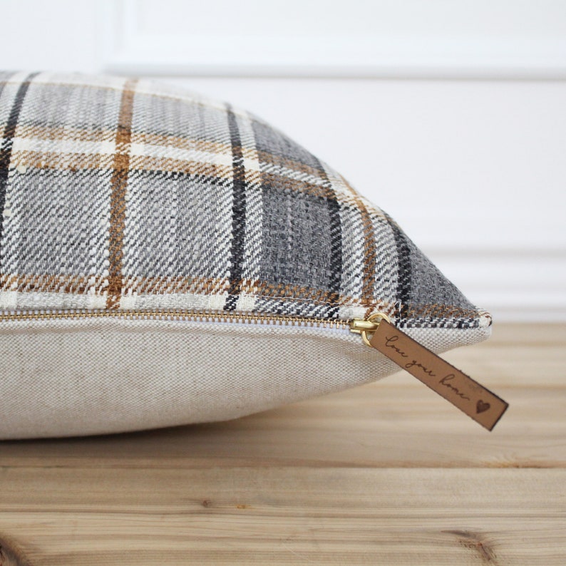 May include: A grey and brown plaid cushion with a zipper closure and a brown leather tag that says "Love you home" with a heart.