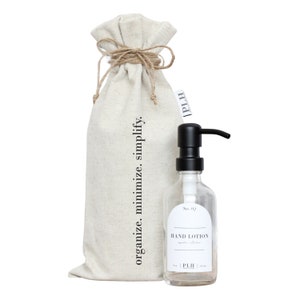 May include: A white canvas bag with the text "organize. minimize. simplify." printed on it. The bag is tied with twine and has a small label with the text "PLH". A clear glass bottle with a black pump dispenser and a label that reads "No. 02 HAND LOTION" is next to the bag.