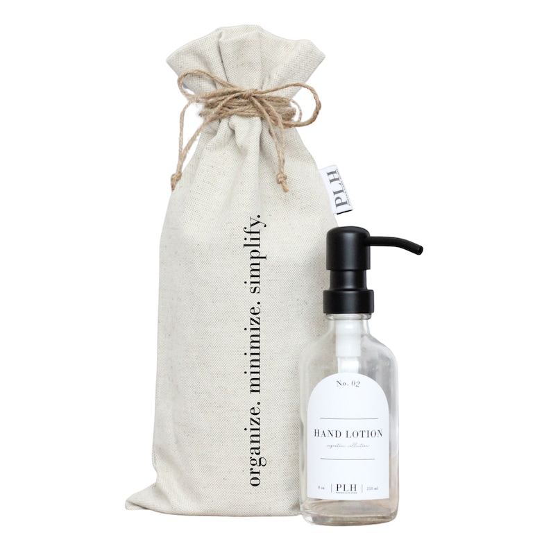 May include: A white canvas bag with the text "organize. minimize. simplify." printed on it. The bag is tied with twine and has a small label with the text "PLH". A clear glass bottle with a black pump dispenser and a label that reads "No. 02 HAND LOTION" is next to the bag.