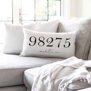 May include: White throw pillow with black text that reads "98275 - Mukilteo, WA". The pillow is on a light grey sofa.