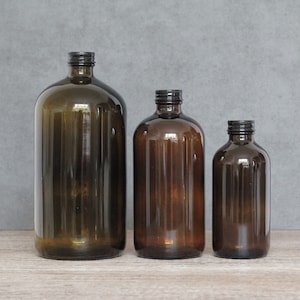 May include: Three amber glass bottles with black lids. The bottles are different sizes and are arranged in a row from largest to smallest.
