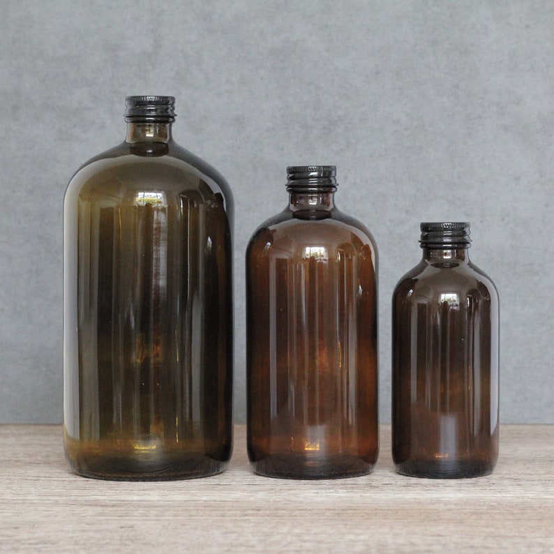 May include: Three amber glass bottles with black lids. The bottles are different sizes and are arranged in a row from largest to smallest.