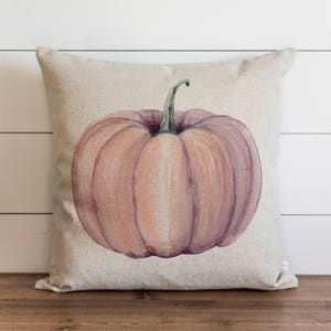 Op de afbeelding: Een decoratief kussen met een aquarel-illustratie van een roze pompoen op een linnen achtergrond.