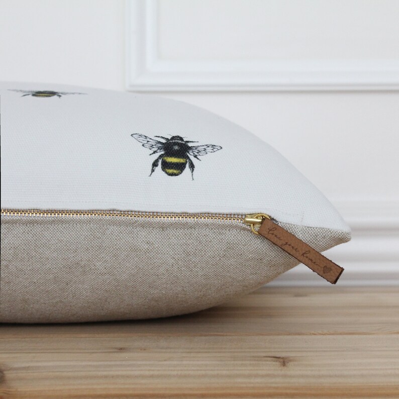 May include: White pillow with a zipper closure and a brown leather tag that says "Love your home". The pillow has a white background with black and yellow bees printed on it.