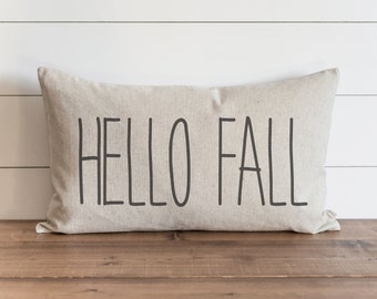 Könnte beinhalten: Ein beiger Kissenbezug mit dem Text "HELLO FALL" in schwarzen Buchstaben.
