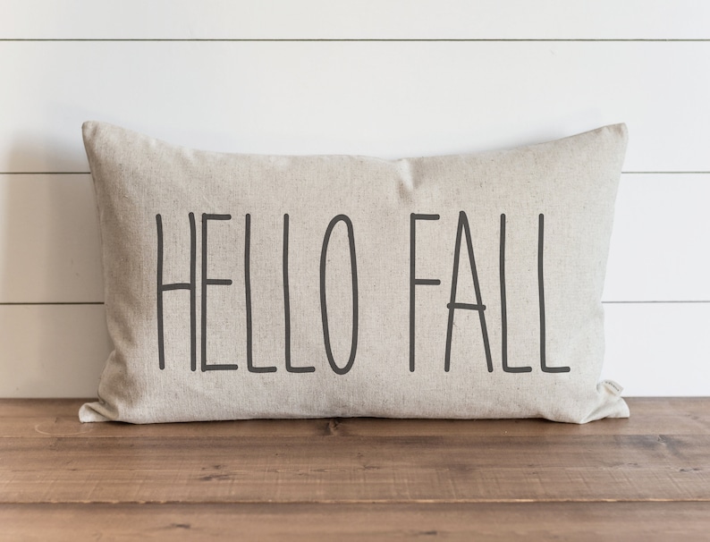 Op de afbeelding: Een beige kussen met de tekst "HELLO FALL" in zwarte letters.