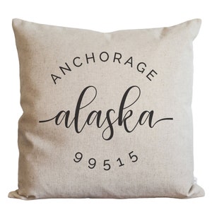 May include: A beige throw pillow with black text that reads "ANCHORAGE alaska 99515".