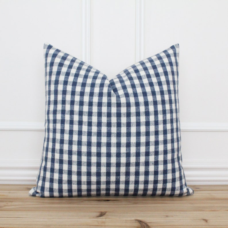 K&ouml;nnte beinhalten: Ein blaues und wei&szlig;es Gingham-Kissenbezug. Der Kissenbezug ist aus einem weichen, gewebten Stoff und hat eine quadratische Form.