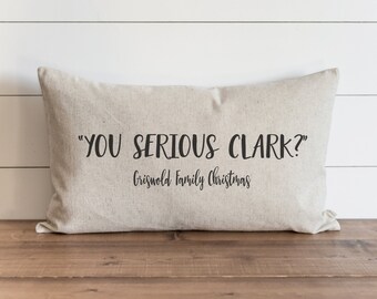 May include: A beige throw pillow with the text "YOU SERIOUS CLARK?" and "Griswold Family Christmas" in black lettering.