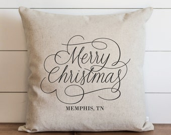 May include: A beige linen throw pillow with black cursive text that reads "Merry Christmas" and "MEMPHIS, TN".
