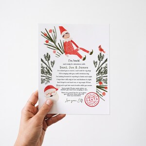 Może przedstawiać: Biała prostokątna kartka z świąteczną ilustracją elfa, Świętego Mikołaja i gałązek iglastych. Tekst głosi: I'm back! and ready for adventures with DANI, JON & JAMES. Zawiera czerwoną okrągłą pieczątkę z napisem North Pole Santa Mail.