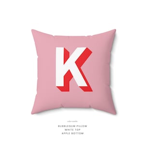Puede incluir: Una almohada rosa con una letra K blanca en un contorno rojo. La almohada est&aacute; etiquetada como "Bubblegum Pillow, White Top, Apple Bottom".