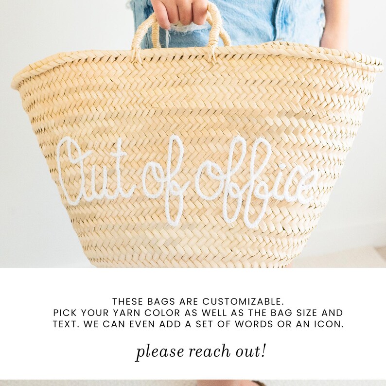 May include: A large, woven straw tote bag with the words "Out of Office" embroidered in white. The bag has two handles and is held by a person wearing denim shorts. The bag is a natural beige color.