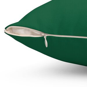 Puede incluir: Una almohada verde oscuro con cierre de cremallera. La cremallera es visible y tiene un tirador de metal.