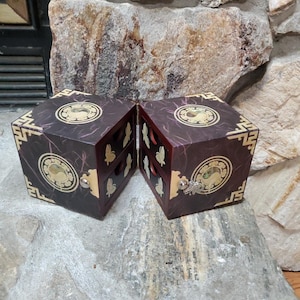 May include: A dark red wooden box with gold accents and a yin yang symbol on the front. The box is open and has two compartments.