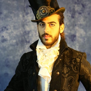 May include: A man wearing a black velvet jacket with a white ruffled collar and a black top hat with clockwork embellishments.