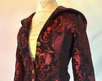 May include: A long, black and red brocade coat with a hood. The coat has a floral pattern and gold buttons.