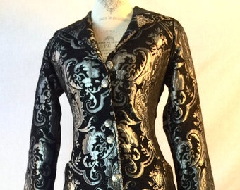 May include: A long black and silver brocade coat with a button-up front and long sleeves. The coat has a paisley pattern.