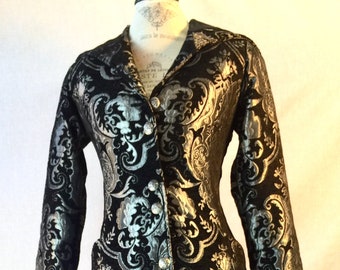 May include: A long black and silver brocade coat with a button-up front and long sleeves. The coat has a paisley pattern.