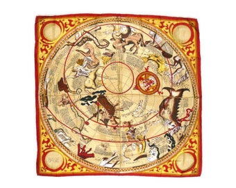 May include: Square silk scarf featuring a celestial map design. The scarf has a cream-colored background with illustrations of constellations, planets, and figures. It is bordered by a red frame with gold decorative elements. The word "BASE" is visible in the corner.