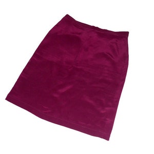 Puede incluir: Una falda lápiz de color magenta. La falda está hecha de un material liso, posiblemente satén o terciopelo. La falda tiene un corte recto, a la altura de la rodilla y un diseño sencillo.