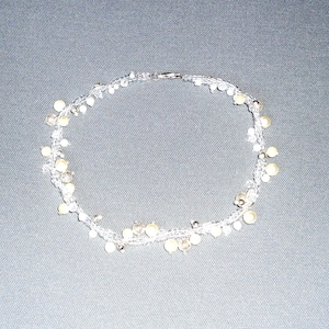 Może przedstawiać: Delikatny naszyjnik z przezroczystych koralików i małych, kremowo-białych pereł. Naszyjnik jest nawleczony na przezroczysty sznurek i ma srebrne zapięcie. Projekt ma kształt okrągły.