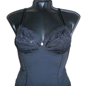 May include: Black bodysuit with lace detailing on the bust. The lingerie features adjustable straps and a small decorative accent at the center. The garment is displayed on a black mannequin.