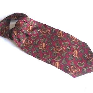 Puede incluir: Corbata tipo ascot burdeos con un estampado repetido de rosas y formas de cachemira en tonos marrón y verde oliva. La corbata es de material sedoso y se muestra sobre un fondo blanco.