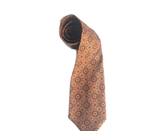 May include: A rolled-up necktie with a repeating geometric pattern in shades of brown, tan, and orange. The tie is made of a smooth fabric and is displayed against a white background.