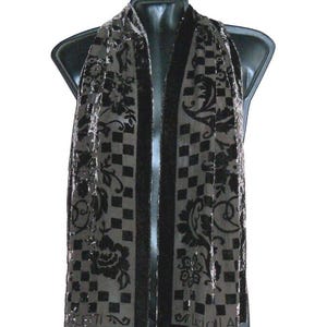 May include: A black and gray scarf with a floral and checkered pattern. The scarf is draped over a black mannequin. The scarf has a dark border and a repeating floral design.