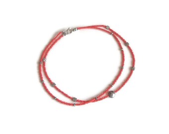 May include: A delicate, double-strand necklace featuring small, vibrant red beads. The necklace is accented with small, silver-colored square and round beads. The clasp is silver-toned. The necklace is displayed on a white background.