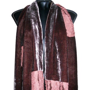 May include: A dark brown velvet scarf with a contrasting pink knitted section. The scarf is draped over a black mannequin, showcasing its texture and design. The scarf's rich color and soft texture are prominent.