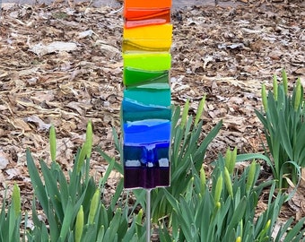 May include: A rainbow glass garden stake with a metal rod. The stake is made of layered glass in the colors of the rainbow, from red to purple.