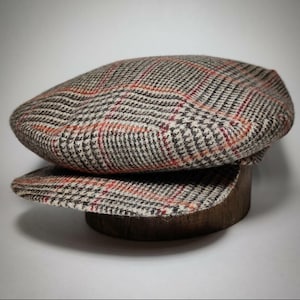 May include: A brown and beige plaid newsboy cap with red accents. The cap is made of wool and has a classic style.