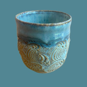 May include: A blue ceramic mug with a textured, gold-colored design. The mug has a wide, rounded shape and a slightly flared lip.