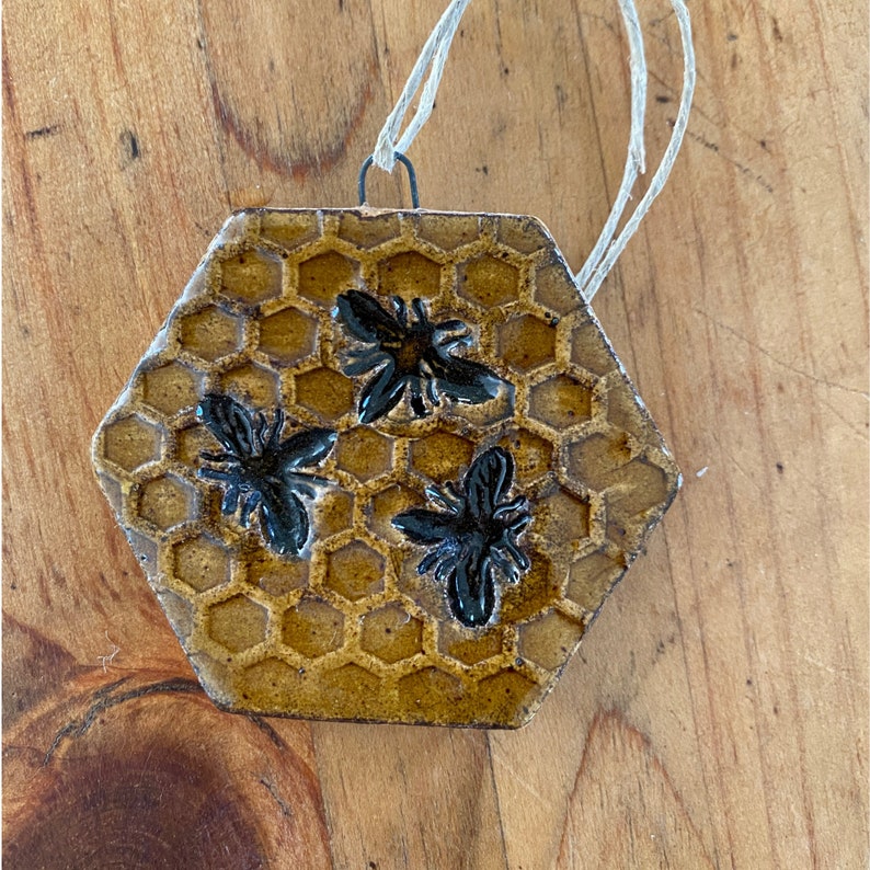 May include: A ceramic honeycomb ornament with three black bees. The ornament is brown and gold and has a string for hanging.