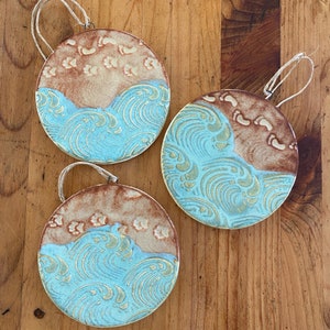 May include: Three ceramic ornaments with a blue and brown wave design. The ornaments are round and have a rustic, handmade look.