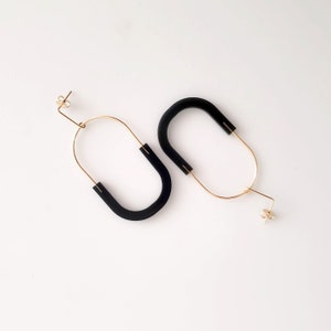 May include: A pair of black and gold hoop earrings. The hoops are made of thin gold wire and have a black rubber oval shape attached to them.