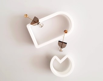 May include: Two pairs of earrings with geometric shapes and clear glass beads. The earrings are displayed on a white background.
