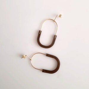 May include: A pair of gold hoop earrings with a dark brown, semi-circular, resin accent.