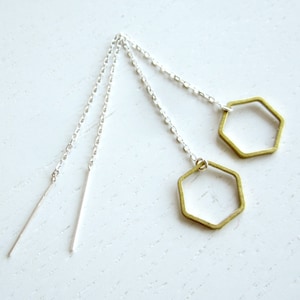 May include: A pair of silver chain earrings with gold hexagon charms. The charms are hollow and have a geometric design.