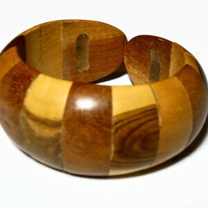 May include: A wooden bracelet with a segmented design. The bracelet is made of various shades of brown wood, creating a checkered pattern. The bracelet is open at one end, allowing it to be put on and taken off.
