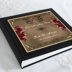 Könnte beinhalten: Schwarzes Hochzeitsalbum mit goldener Umrandung und braunem Einband mit zwei Drachen, roten Rosen und dem Text "Our Wedding Day Zoe & Fergus 10th December 2022".