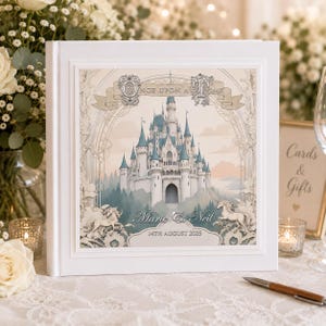 May include: A square white guest book featuring a central illustration of a fairy tale castle with blue turrets. The text reads Once Upon A Time, Marie & Neil, and 14th August 2025. Two white horses are depicted at the base of the castle illustration.