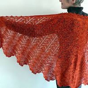 Puede incluir: Un chal de punto de color óxido con un patrón de encaje. El chal está drapeado sobre los hombros y los brazos de una persona.