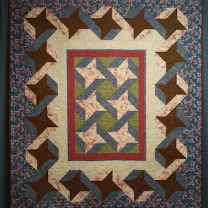 May include: A quilt with a brown, blue, and green star pattern. The quilt is framed by a border of floral fabric.