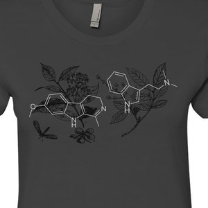 May include: A dark gray t-shirt with a white graphic of a chemical structure surrounded by floral elements and a dragonfly.