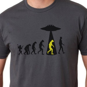 May include: A dark gray t-shirt with a graphic of the evolution of humans, ending with a yellow alien being abducted by a UFO.